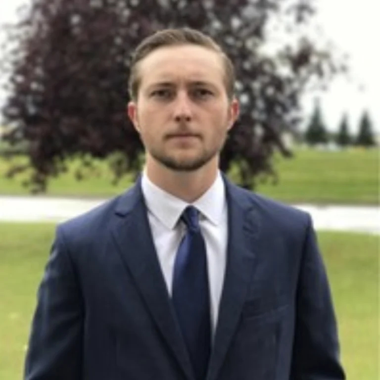 Man in suit standing in a park with a tree in the background