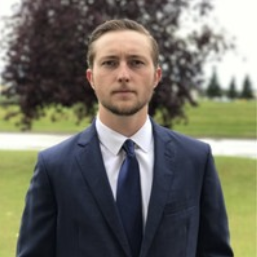 Man in suit standing in a park with a tree in the background