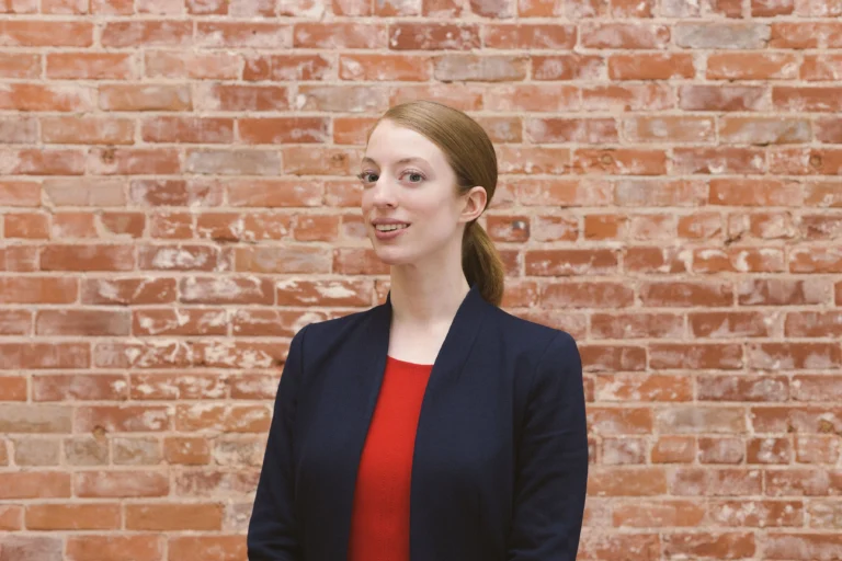 woman in business attire smiling in front of brick wall