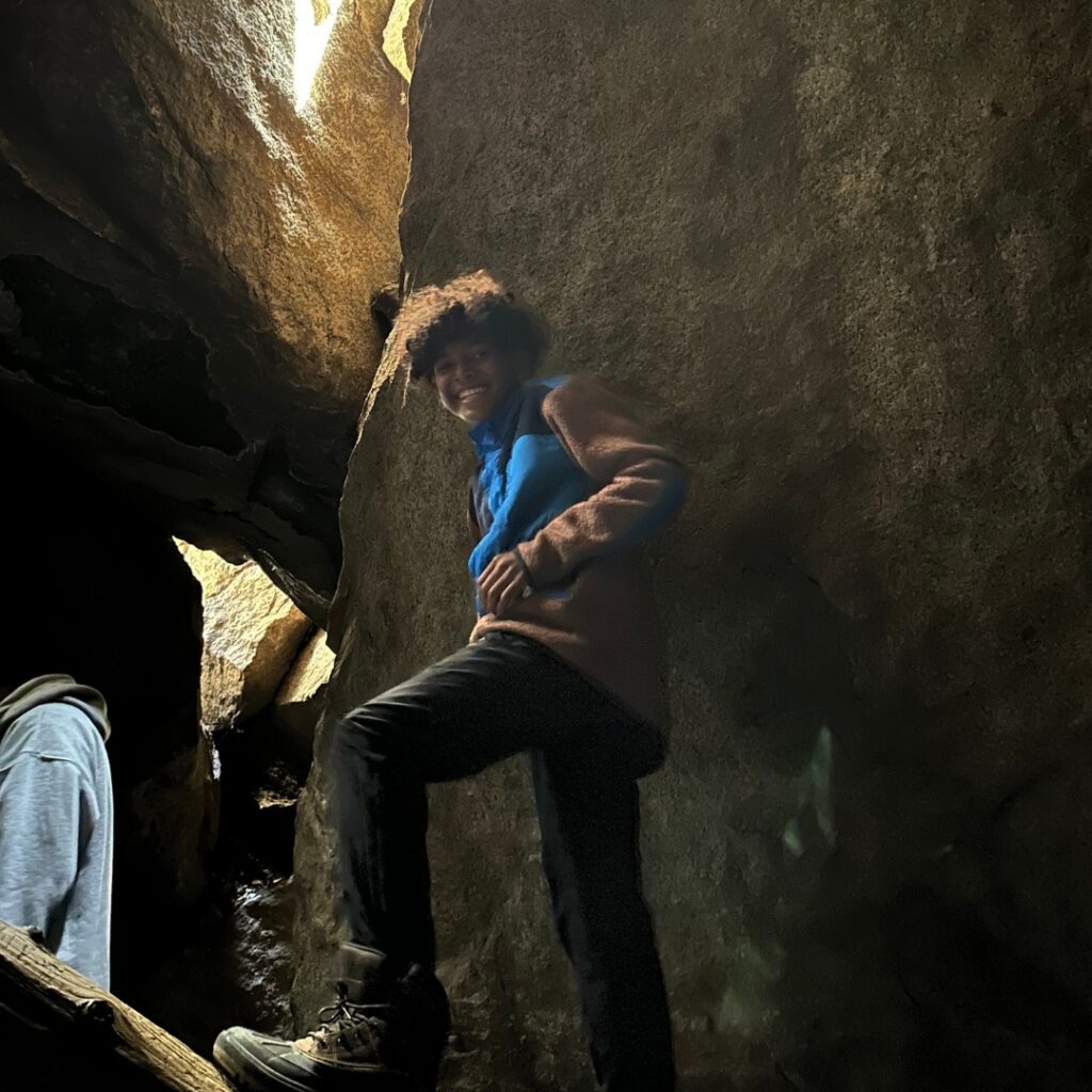 kid standing on branch inside cavern with light peaking through cracks in rock