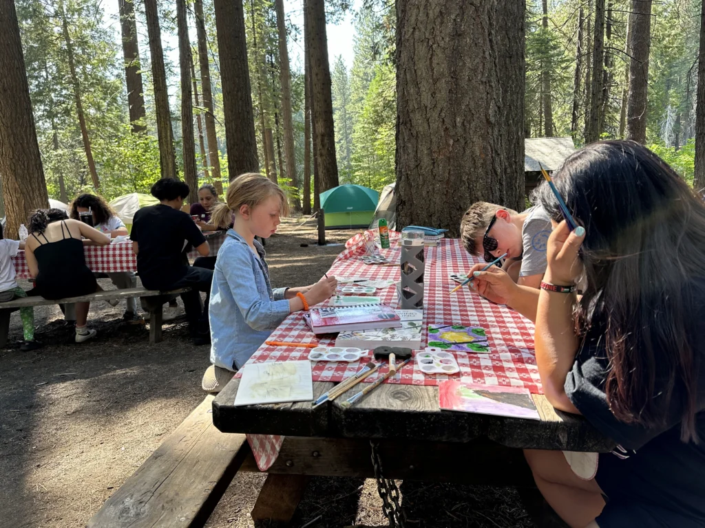 group of kids making water color art at tables on campsite