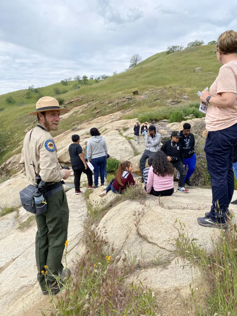 ranger and group hiking across rocks along a grassy hillside