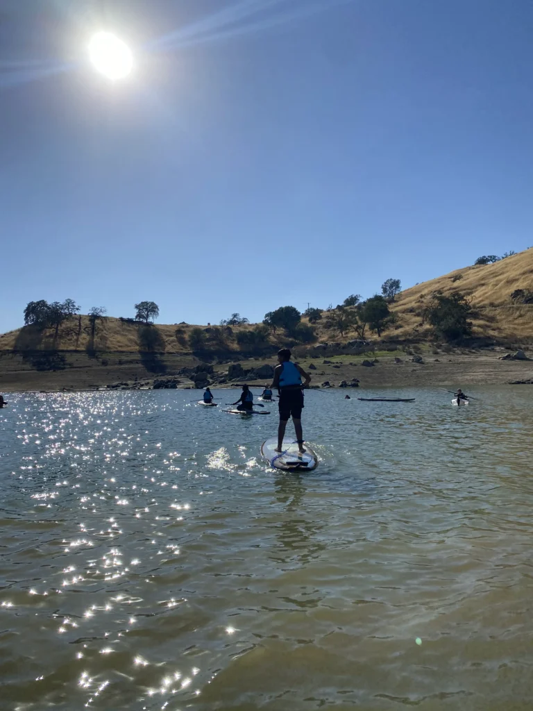 a few kids standing on paddle boards on calm water paddling on lake