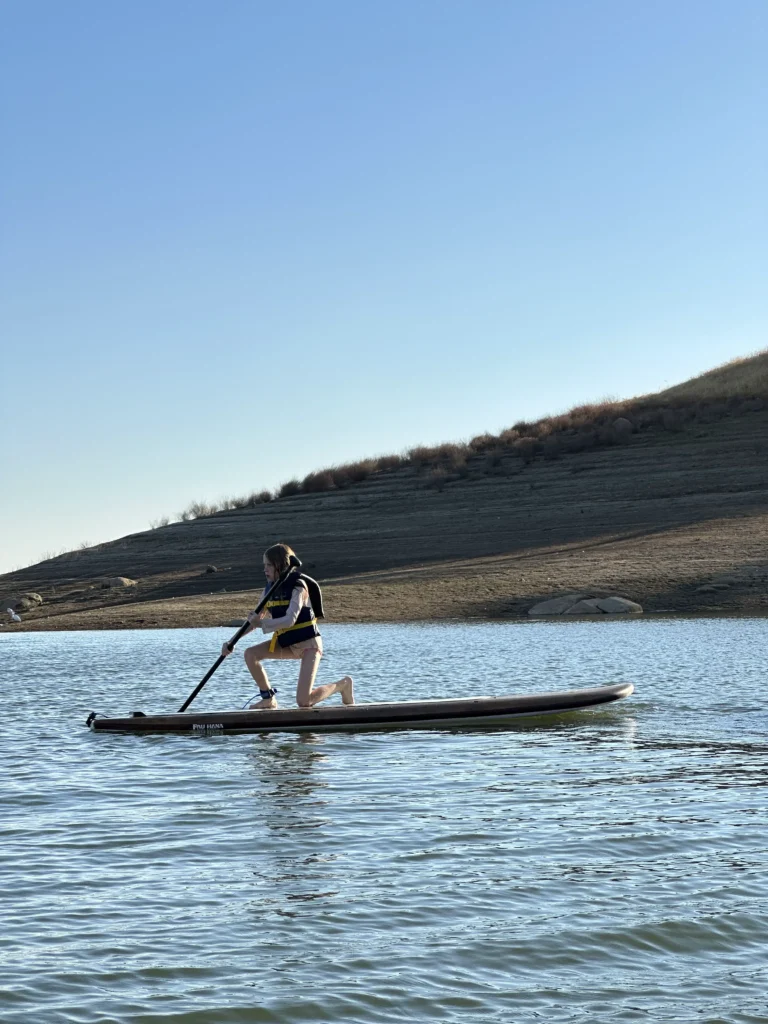 kid kneeling on paddle board paddling on calm water