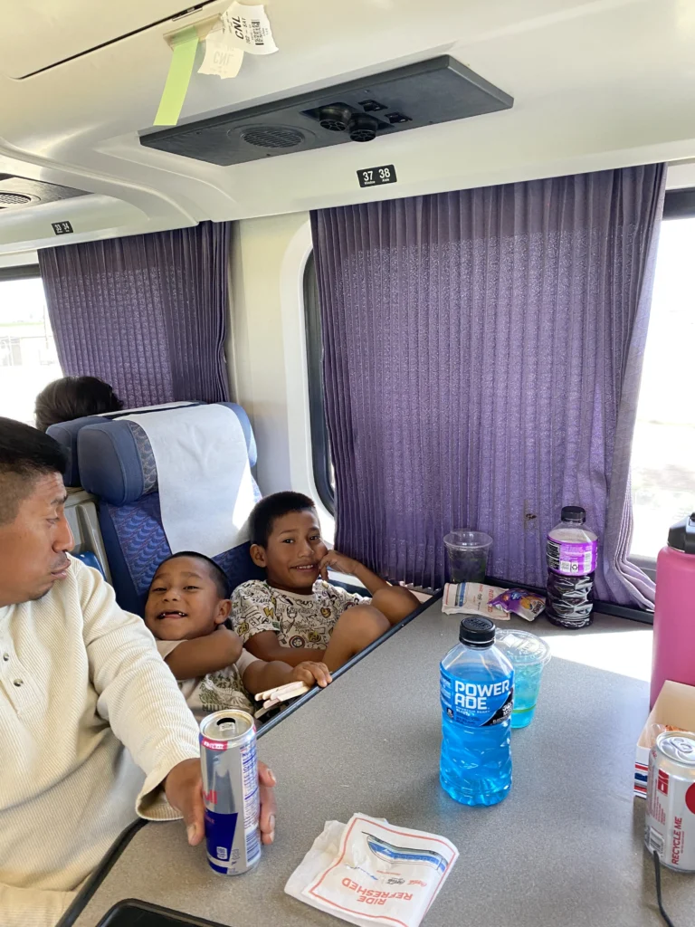 two boys and their father sitting at table with drinks on it aboard a train