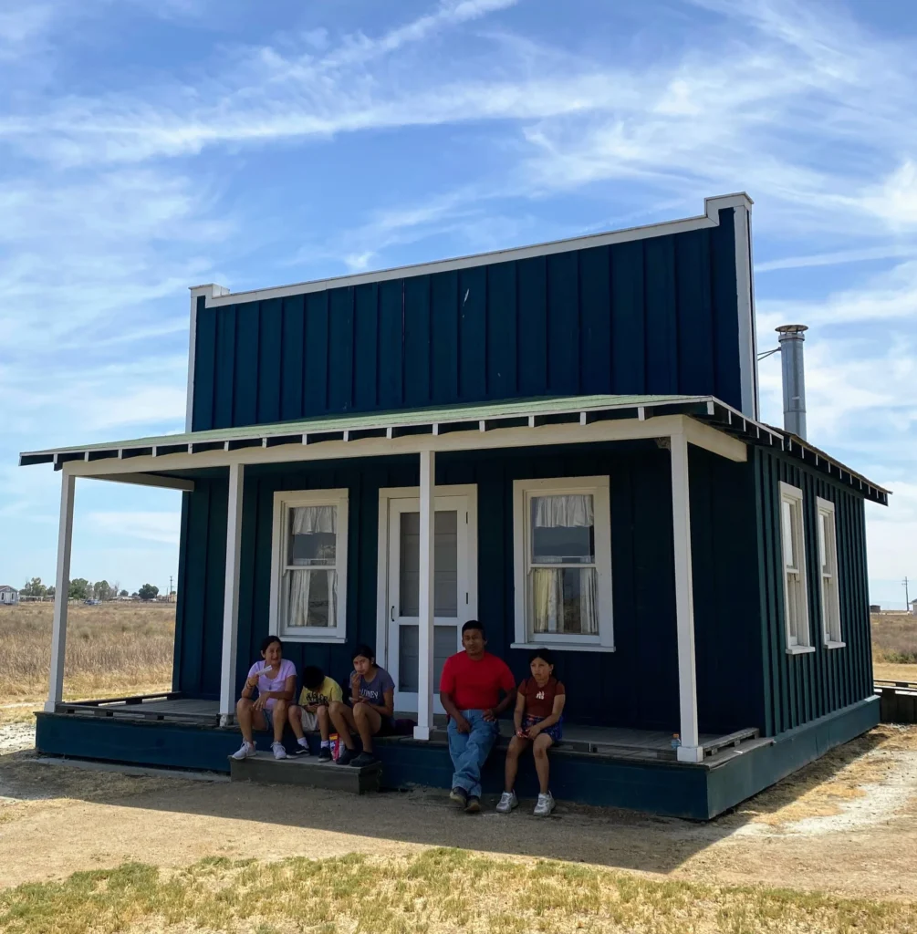 group of five people sitting on porch of historic building in the middle of a field