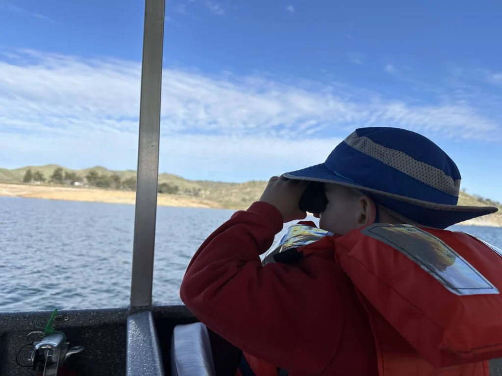 kid looking through binoculars wearing life jacket and hat