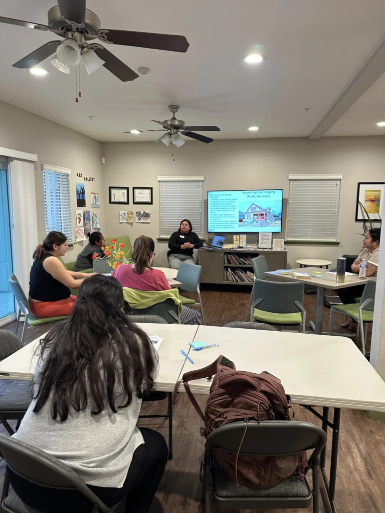 group of people at tables with presenter in front of tv screen