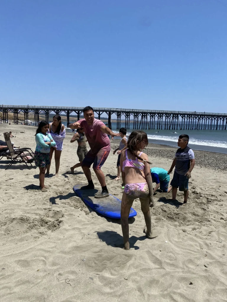 man standing on surfboard in sand demonstrating surf position for kids surrounding