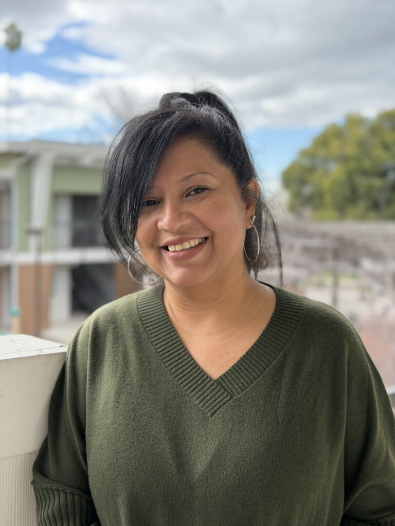 smiling woman in green sweater with blue sky and scattered clouds in background